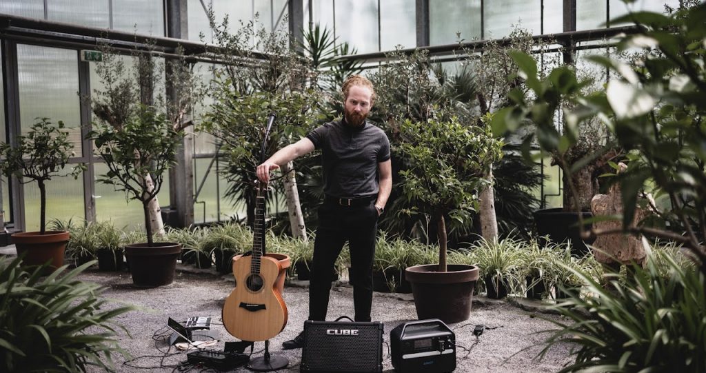 Qukser - Bandmitglied
"Mann im Gewächshaus mit Gitarre und Boxen"